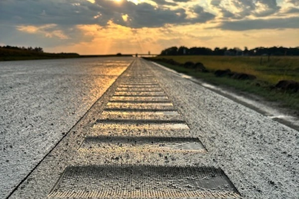 Rumble strips on a wet road with a setting sun in the background